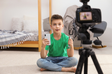 Cute little blogger with phone and selfie stick recording video at home
