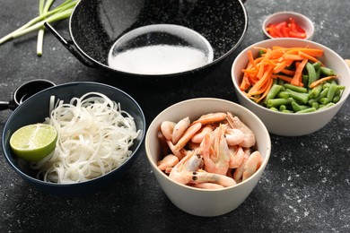 Photo of Shrimps, vegetables, noodles and black wok on grey textured table, closeup