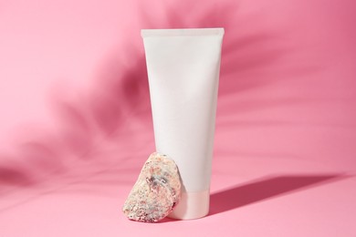 Cosmetic product, quartz gemstone and shadow of tropical leaf on pink background
