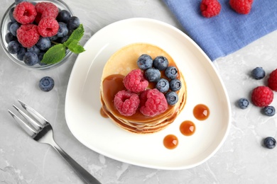 Tasty pancakes with berries and syrup on light grey marble table, flat lay