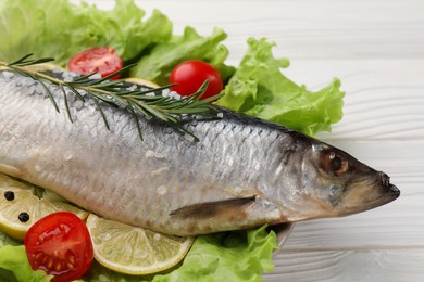 Delicious salted herring, rosemary, lettuce, tomatoes and lemon on white wooden table, closeup