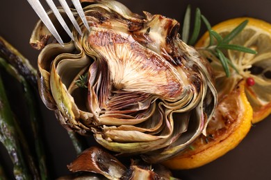 Tasty grilled artichoke and fork on plate, closeup