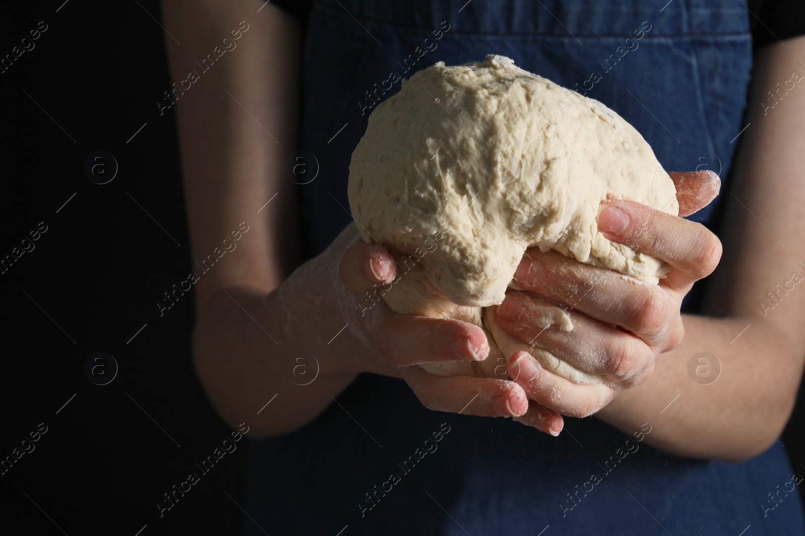 Photo of Making bread. Woman holding dough on dark background, closeup. Space for text