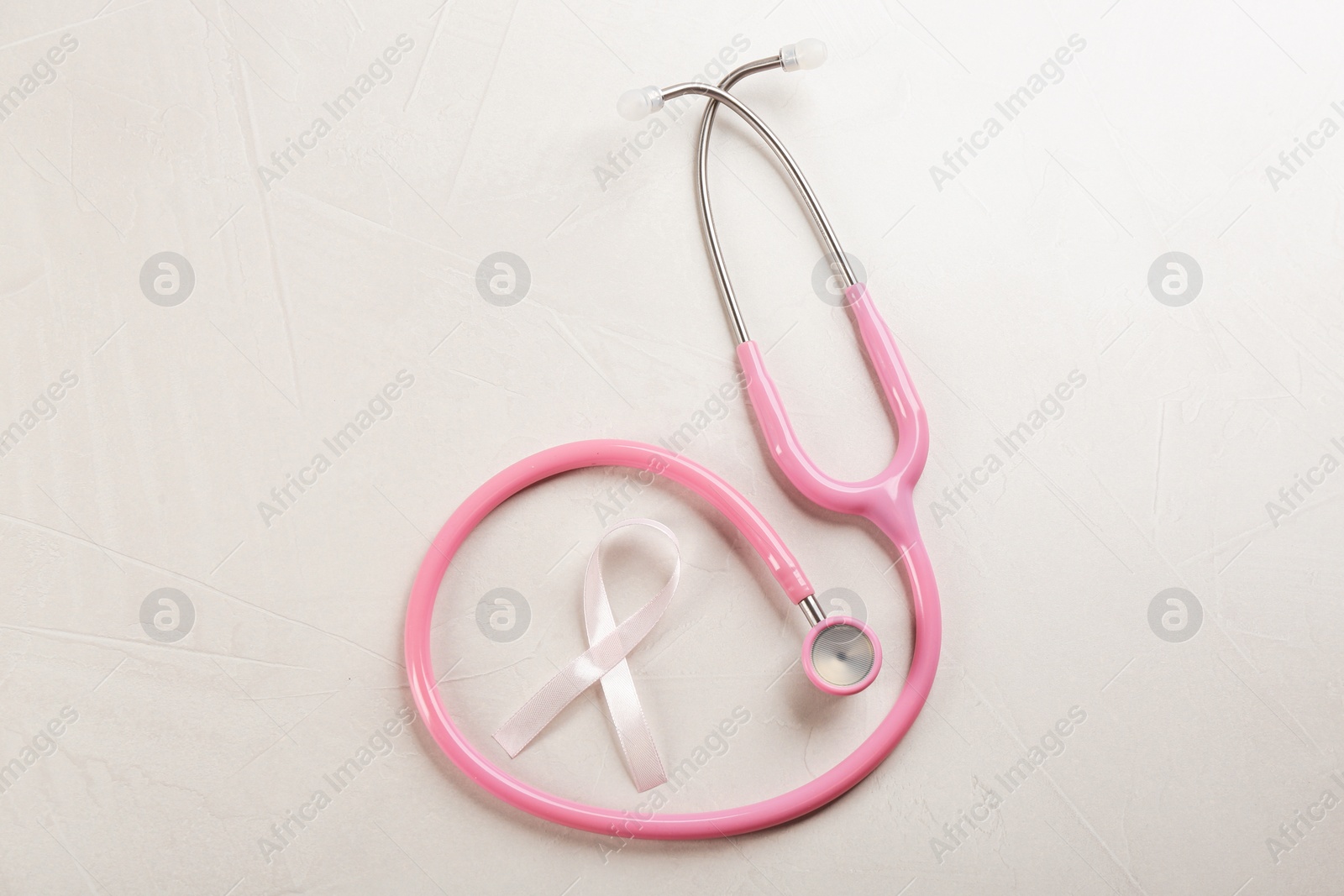 Photo of Pink ribbon and stethoscope on light grey stone background, flat lay. Breast cancer concept