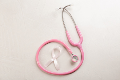 Photo of Pink ribbon and stethoscope on light grey stone background, flat lay. Breast cancer concept