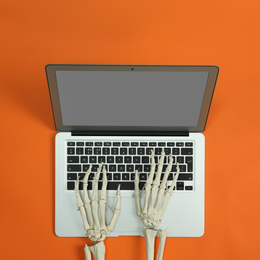 Human skeleton using laptop on orange background, top view