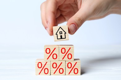 Mortgage rate. Woman building pyramid of cubes with house icon and percent signs at white wooden table, closeup