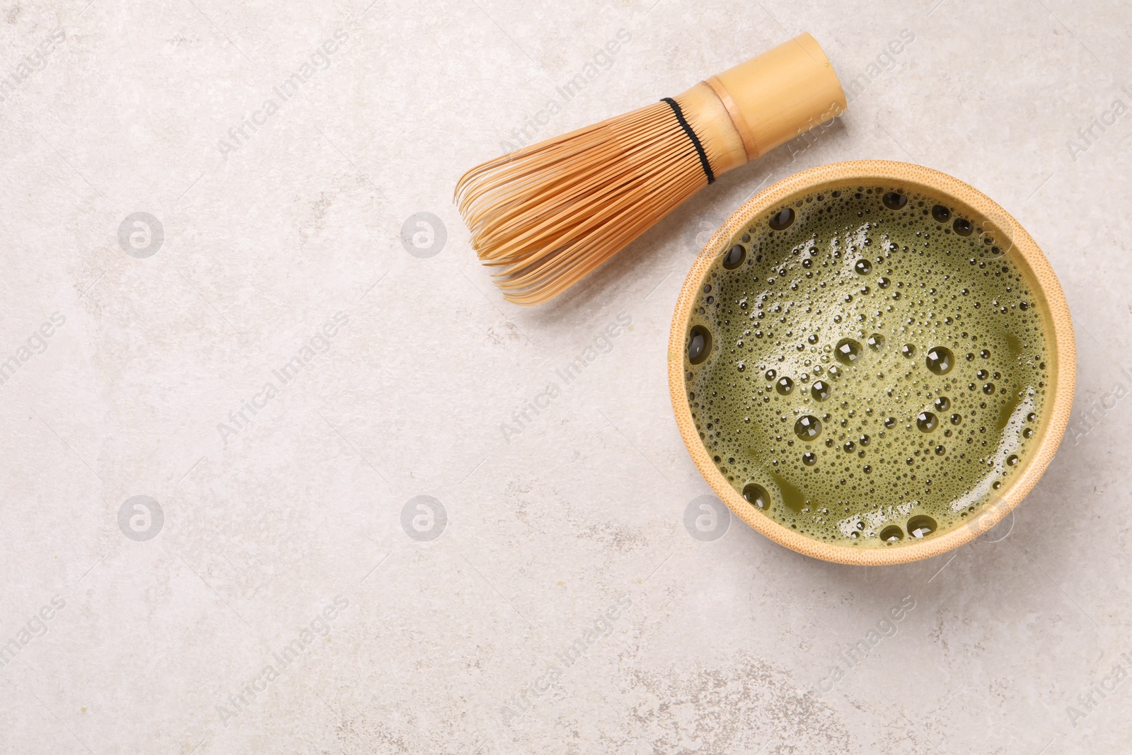 Photo of Bowl of fresh matcha tea and bamboo whisk on light table, flat lay. Space for text