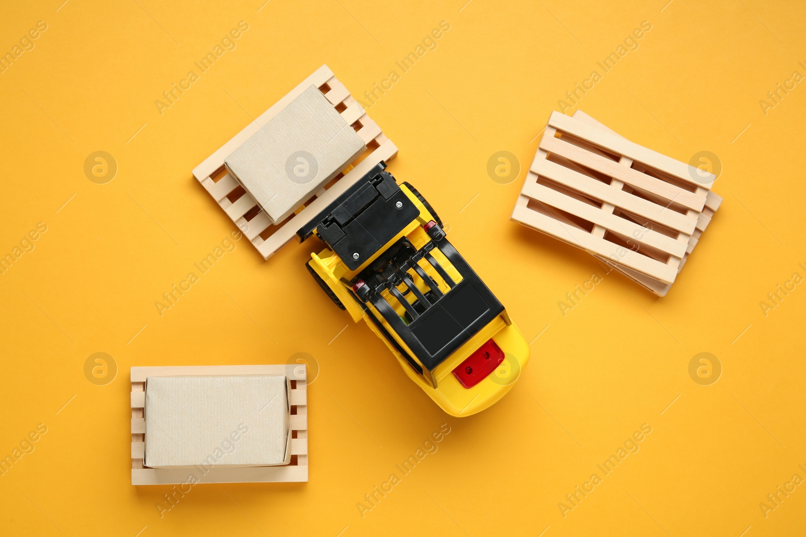 Photo of Toy forklift, wooden pallets and boxes on orange background, flat lay