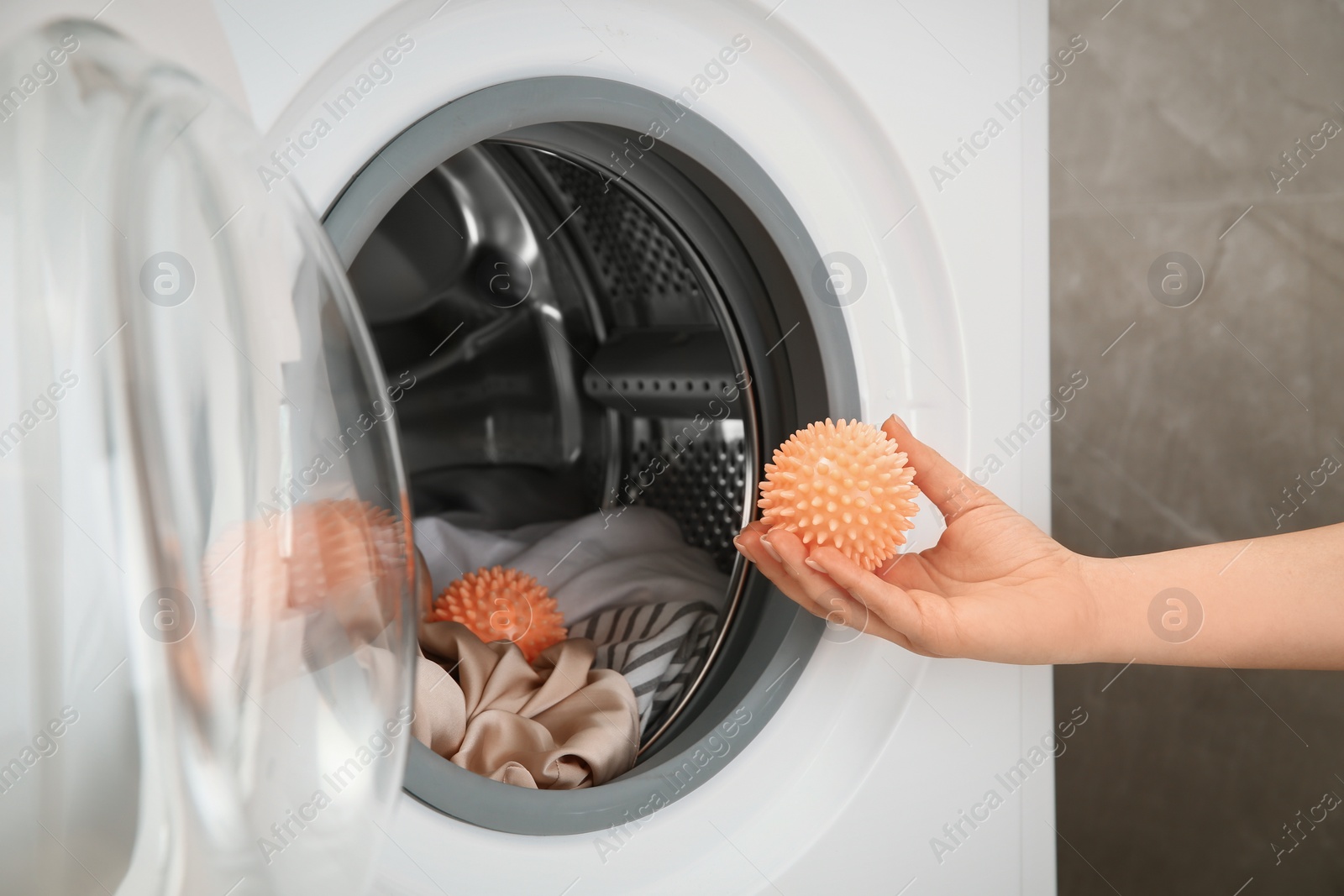 Photo of Woman putting dryer ball into washing machine, closeup