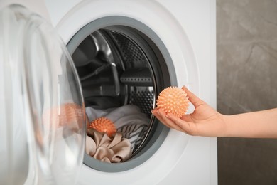 Photo of Woman putting dryer ball into washing machine, closeup