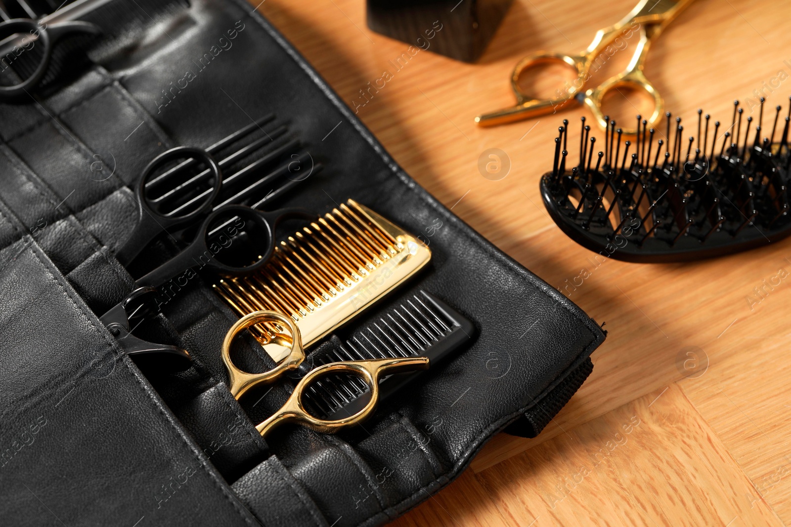 Photo of Hairdresser tools. Professional scissors and combs in leather organizer on wooden table, closeup