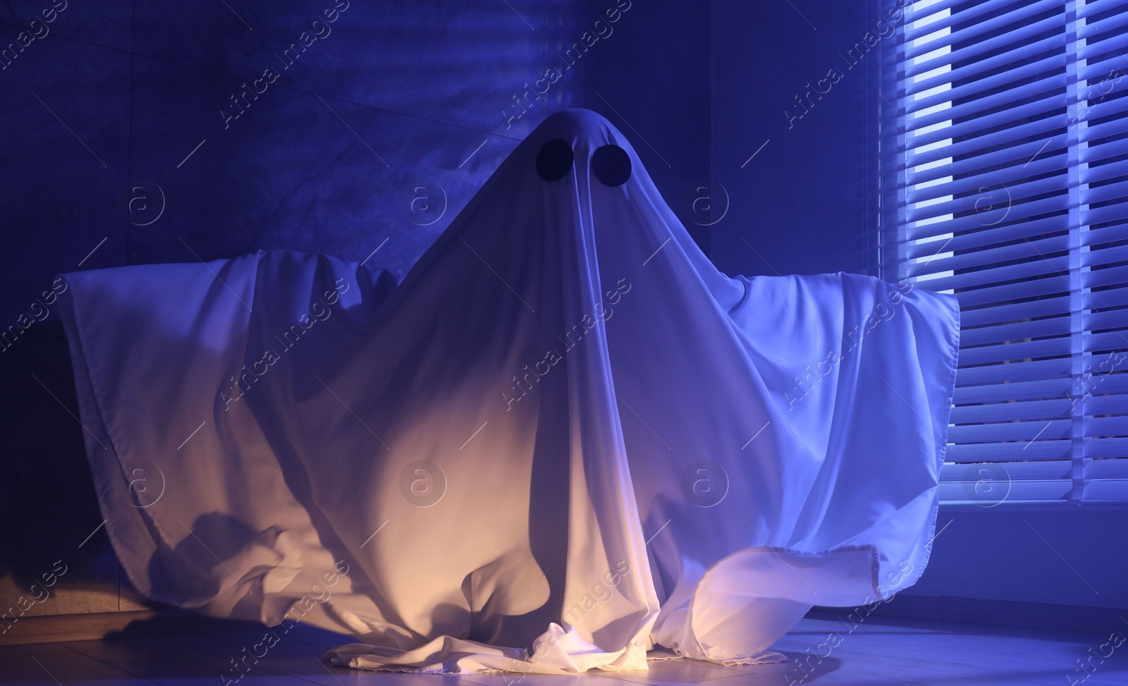 Photo of Creepy ghost. Woman covered with sheet near window in blue light