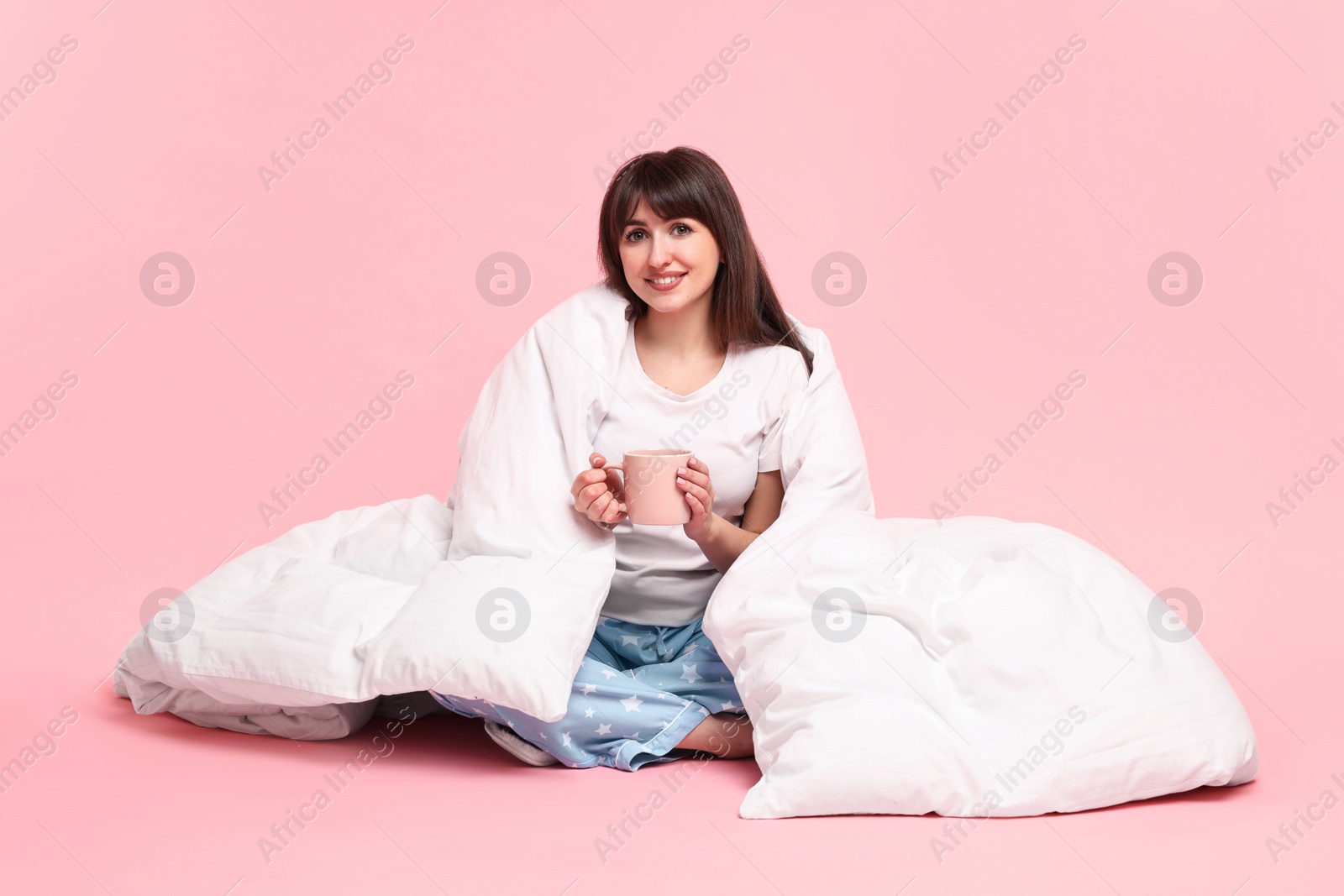 Photo of Happy woman with pyjama and blanket holding cup of drink on pink background