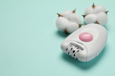 Photo of Modern epilator and fluffy cotton flowers on turquoise background, closeup. Space for text