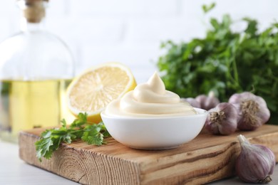 Photo of Tasty mayonnaise sauce in bowl, parsley, garlic and lemon on table, closeup