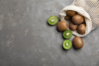 Photo of Net bag with fresh ripe kiwis on grey table, flat lay. Space for text