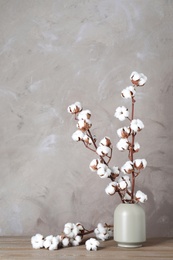 Beautiful cotton flowers in vase on wooden table against beige background. Space for text