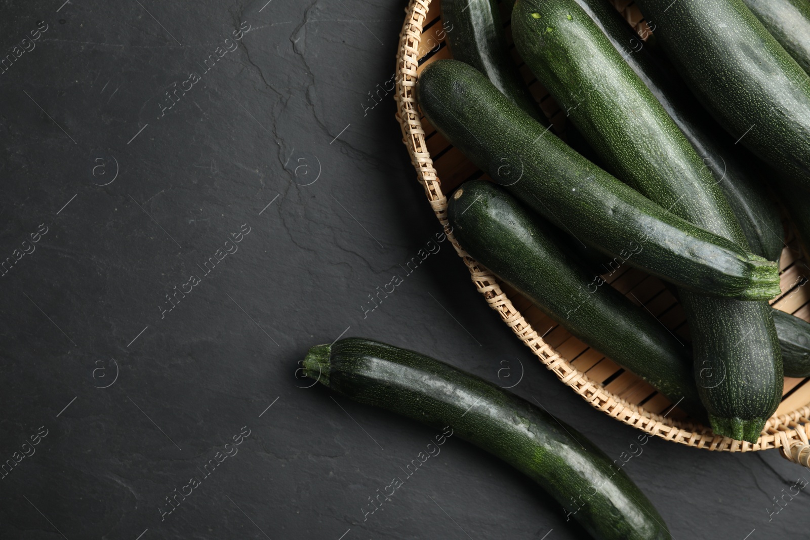 Photo of Basket with green zucchinis on black slate table, flat lay. Space for text