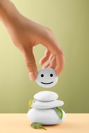 Woman putting stone with drawn happy face on stack, closeup Zen concept