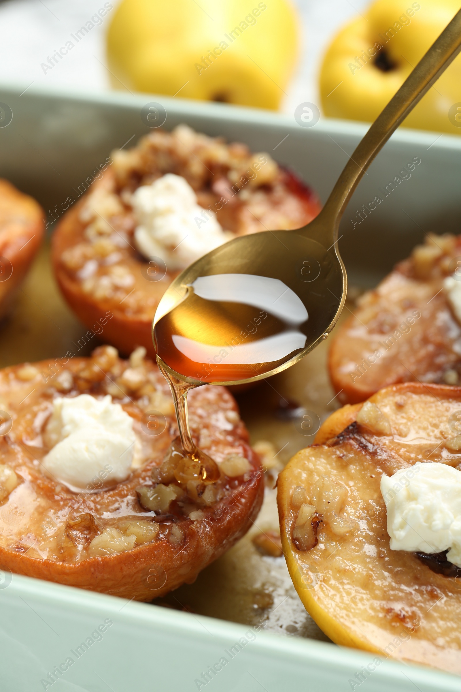 Photo of Pouring honey onto tasty baked quinces with nuts and cream cheese in dish, closeup