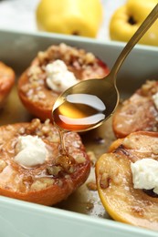 Pouring honey onto tasty baked quinces with nuts and cream cheese in dish, closeup