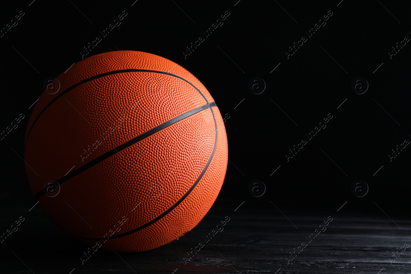 Photo of Basketball ball on black wooden table against dark background, space for text