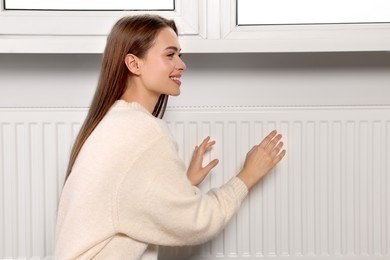 Woman warming hands on white heating radiator indoors