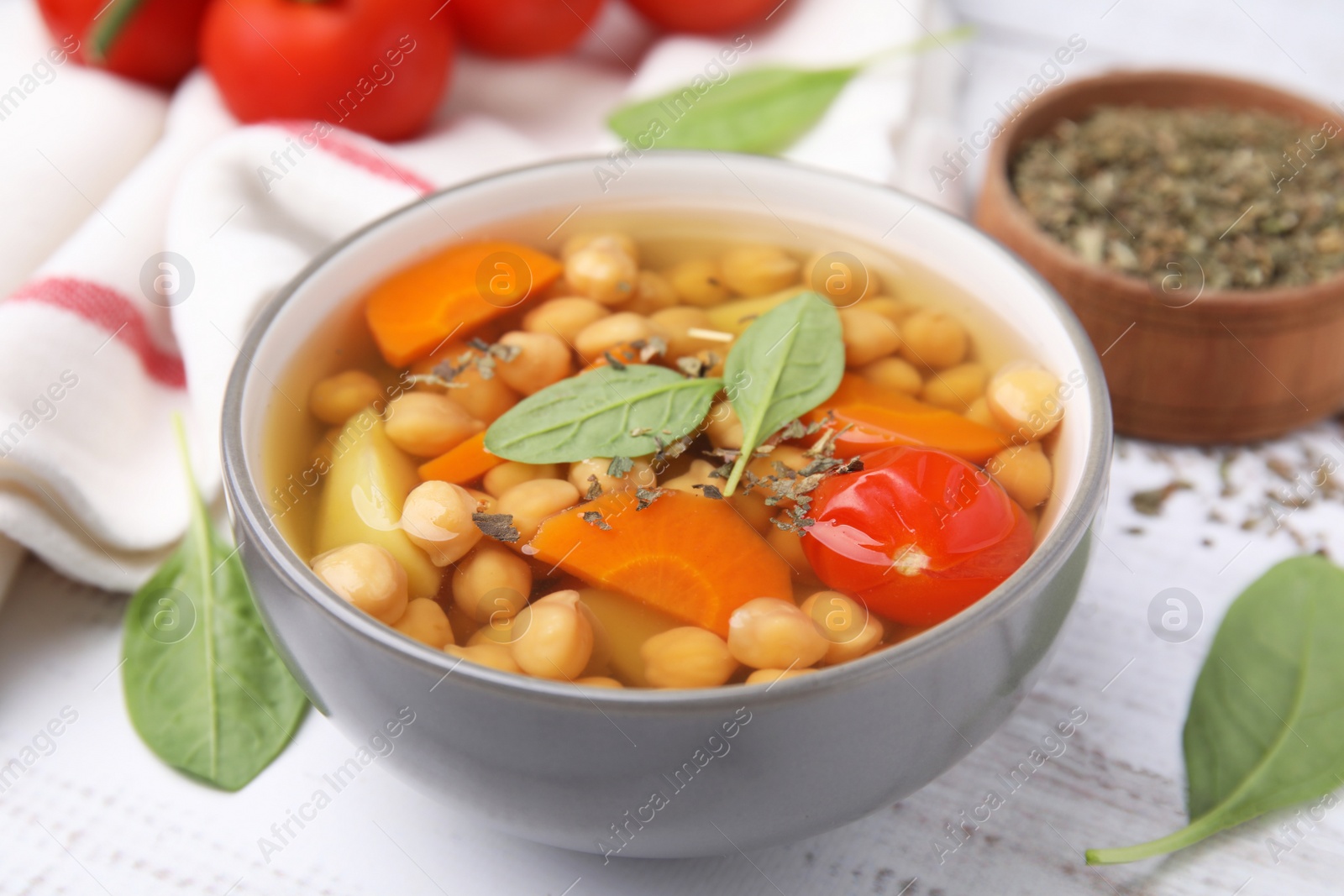 Photo of Tasty chickpea soup in bowl and spices on white wooden table, closeup