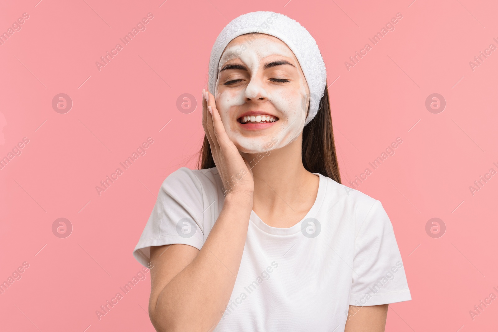 Photo of Young woman with headband washing her face on pink background
