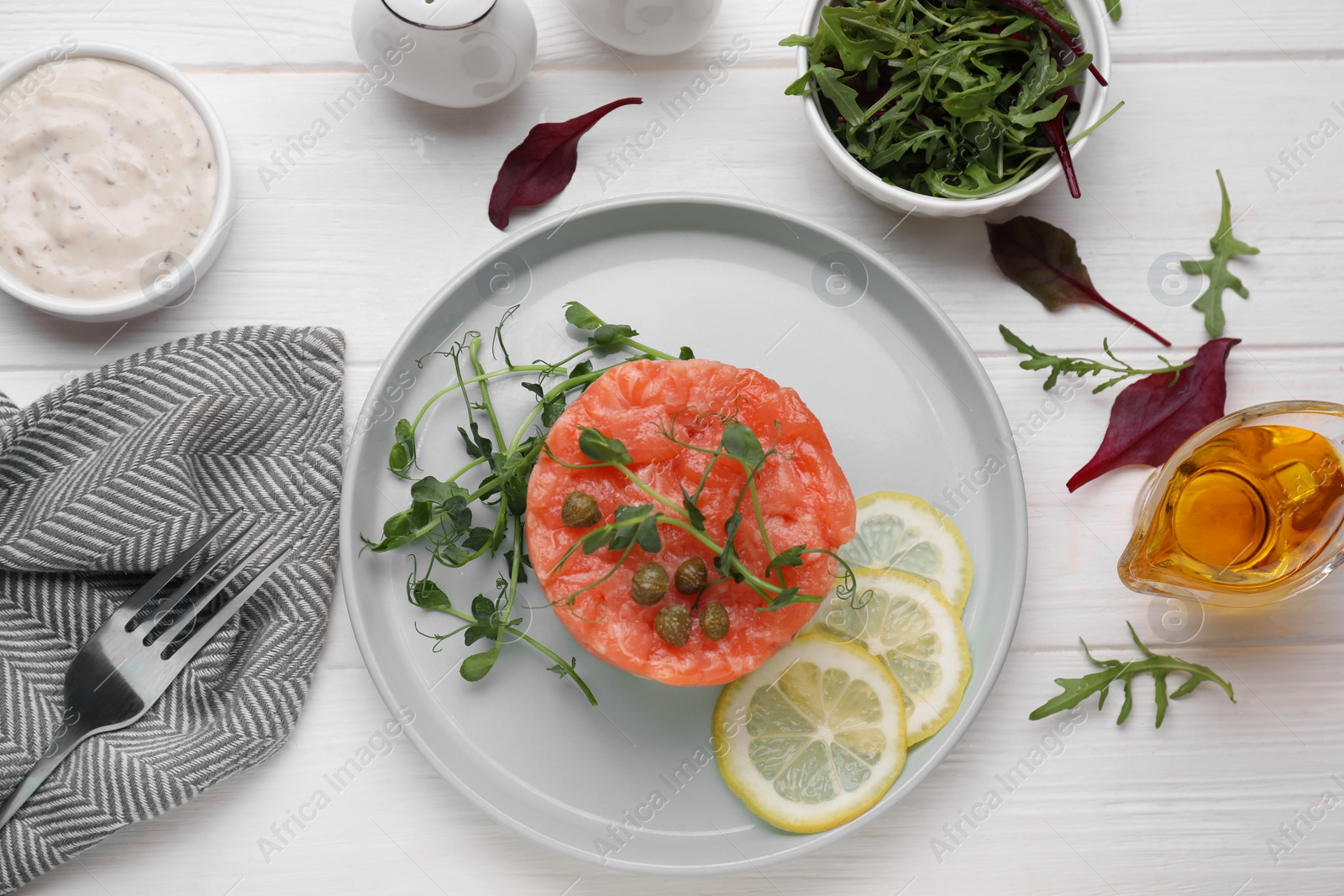 Photo of Tasty salmon tartare with lemon, capers and microgreens served on white wooden table, flat lay