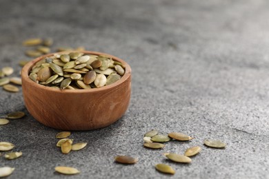 Photo of Wooden bowl with peeled pumpkin seeds on grey table. Space for text