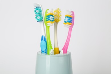 Photo of Different toothbrushes in holder on light grey background, closeup