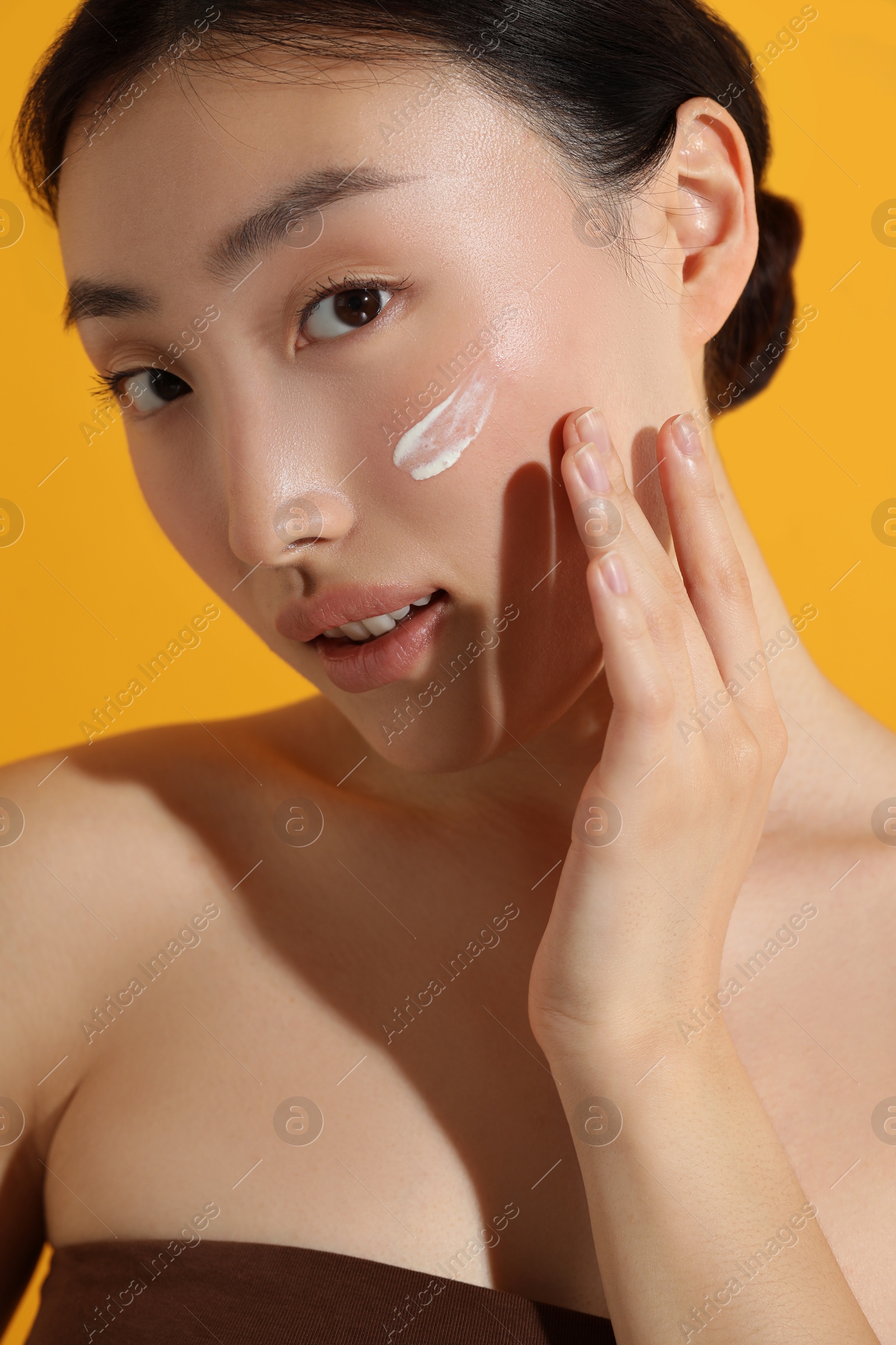 Photo of Beautiful young woman with sun protection cream on her face against orange background