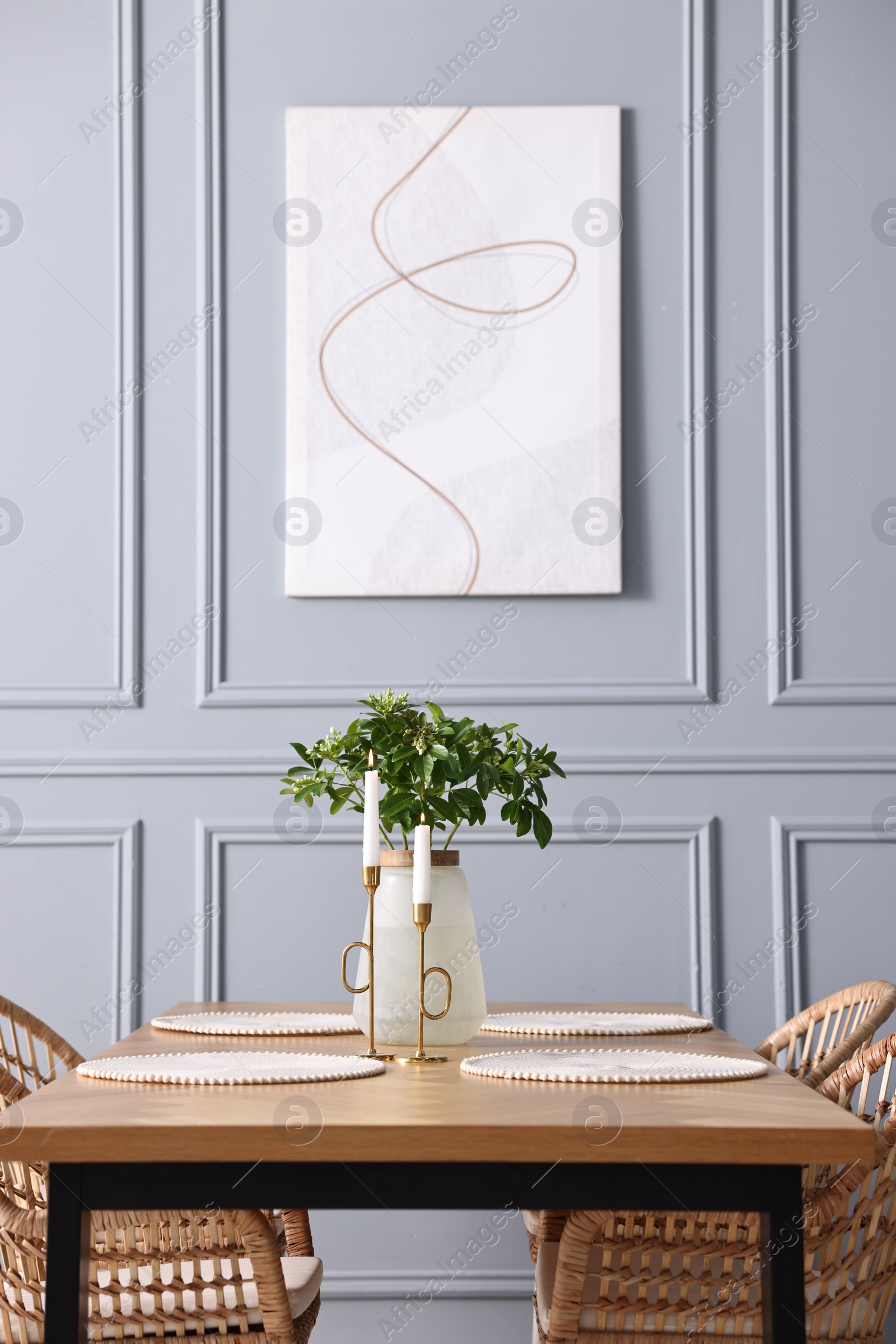 Photo of Rattan chairs, table, burning candles and vase with green branches in stylish dining room