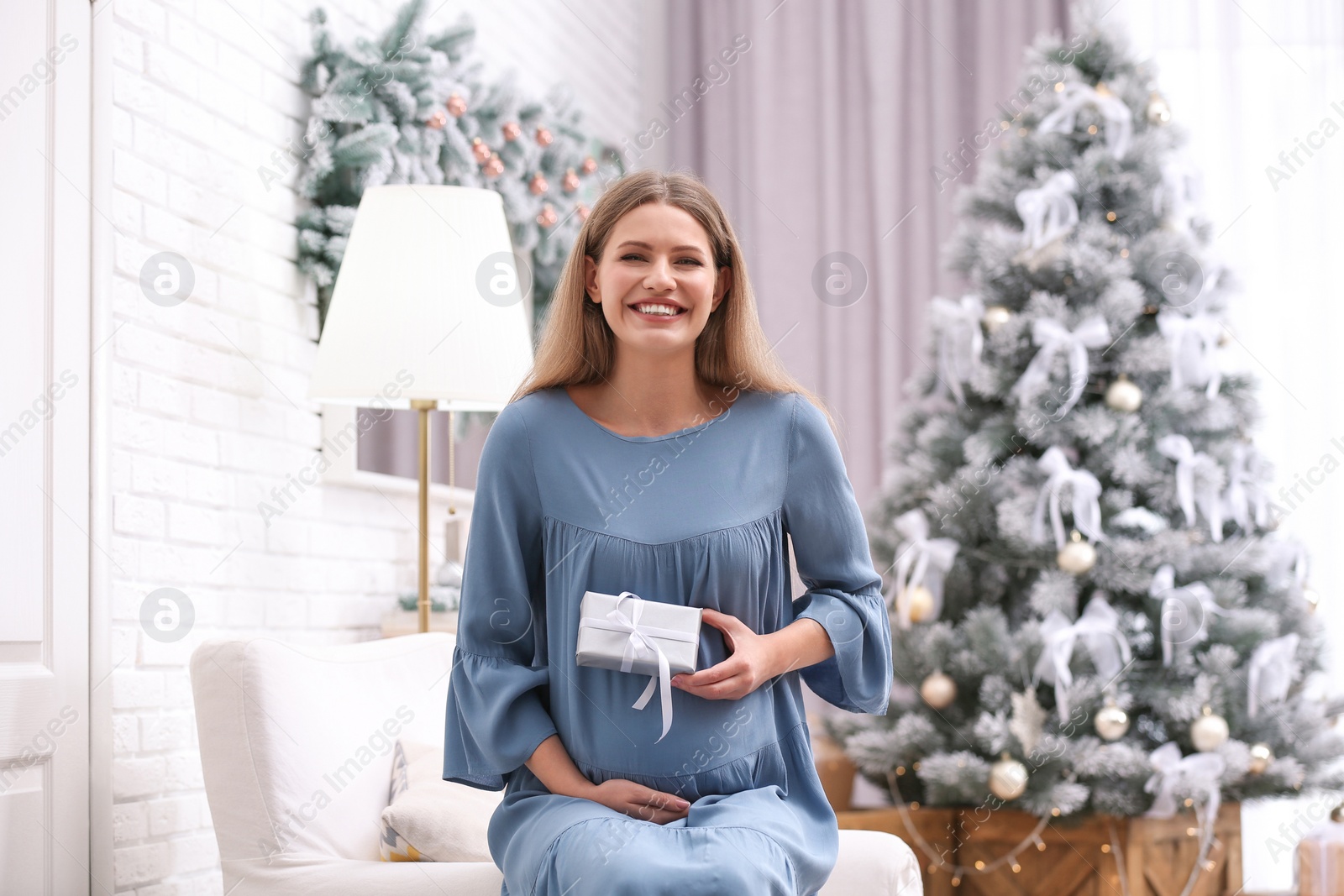 Photo of Young pregnant woman with Christmas gift at home