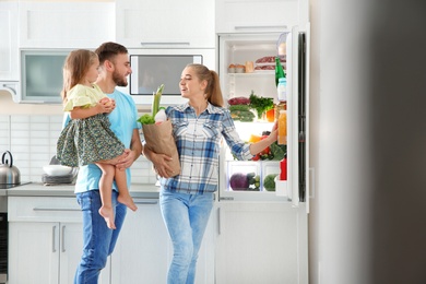 Happy family with paper bag full of products standing near refrigerator in kitchen