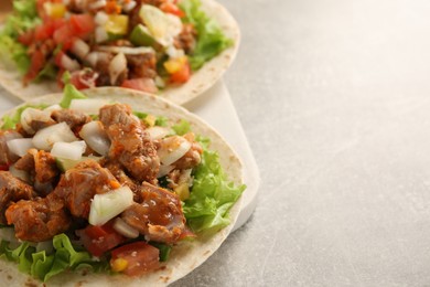 Delicious tacos with vegetables and meat on light table, space for text