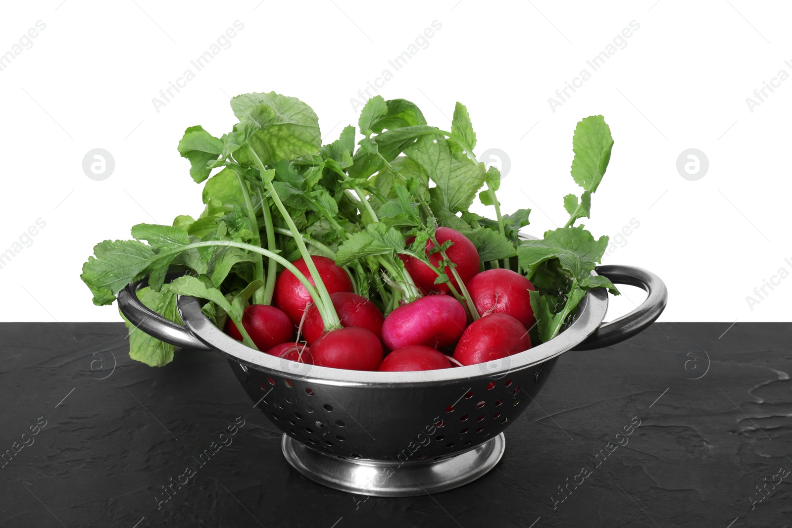 Photo of Metal colander with fresh radishes on black textured table against white background