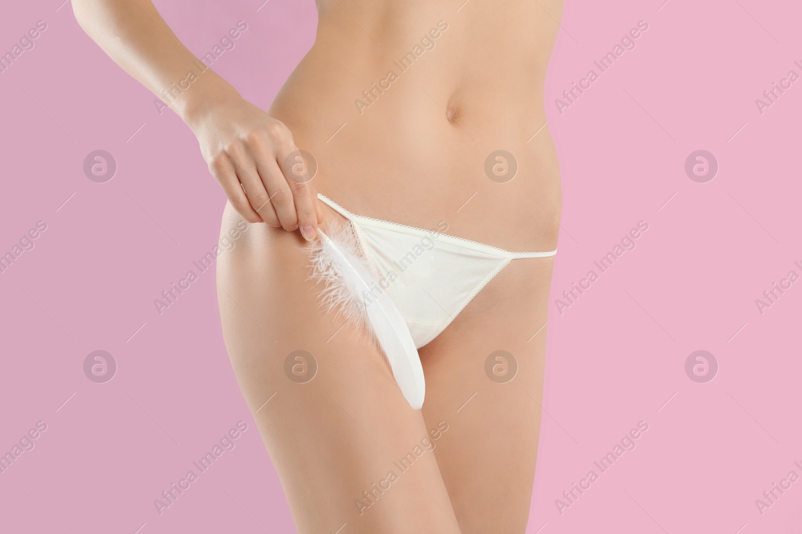 Photo of Woman with feather showing smooth skin after Brazilian bikini epilation on pink background, closeup. Body care concept