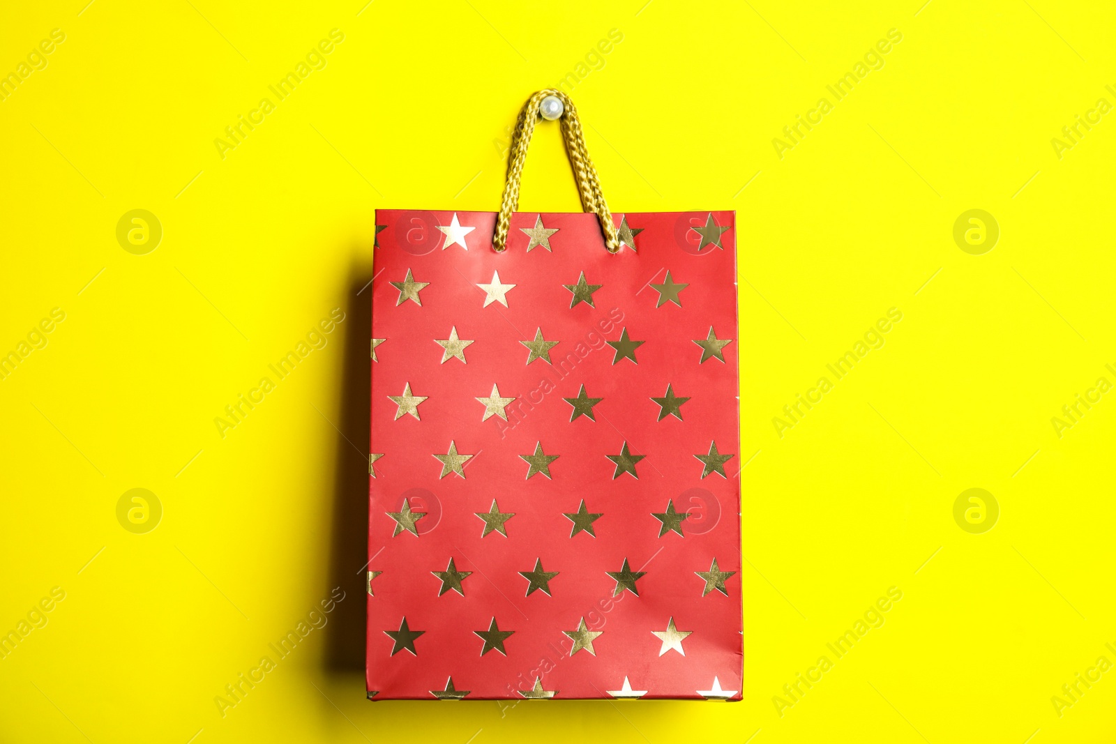 Photo of Red shopping paper bag with star pattern on yellow background