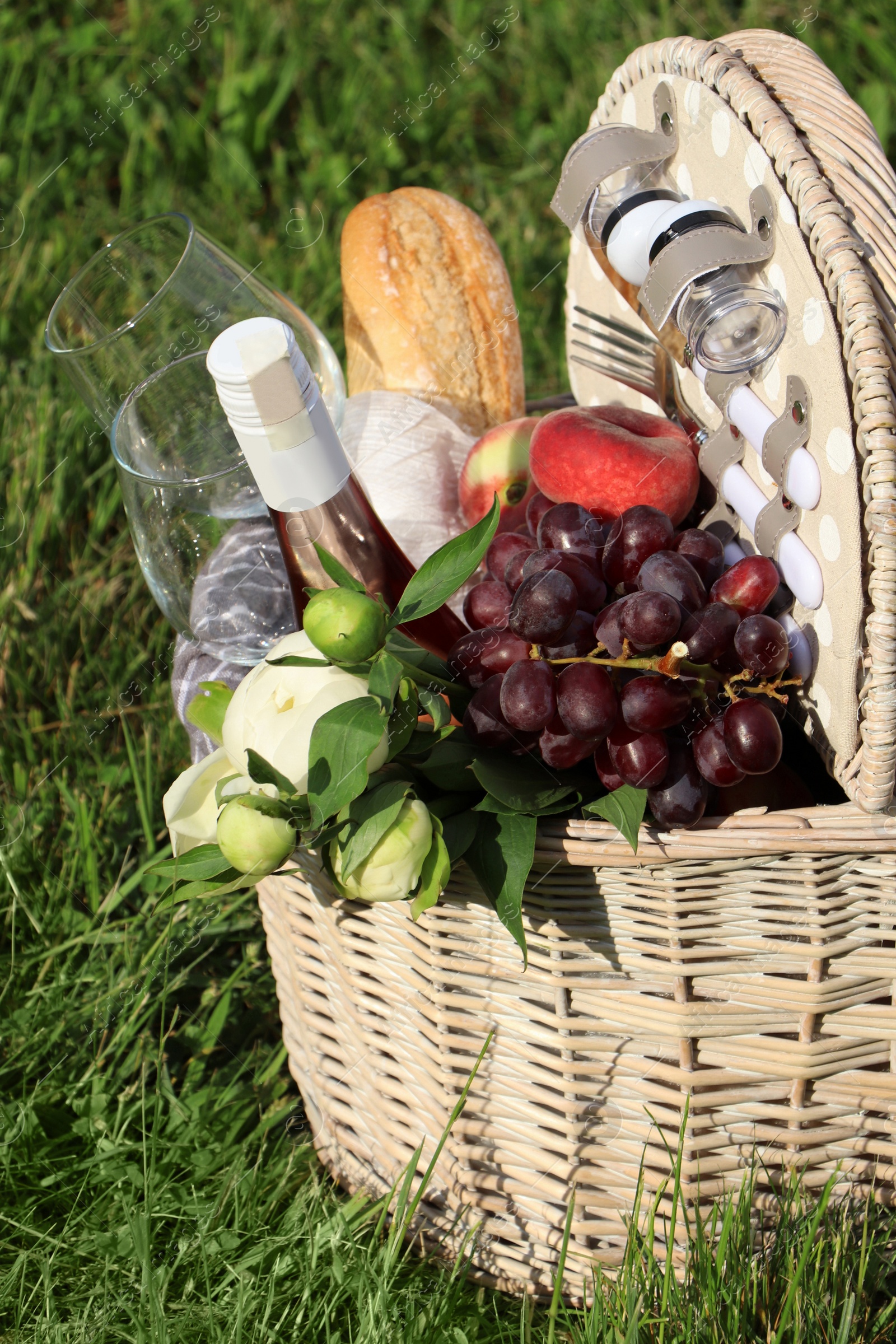 Photo of Picnic basket with tasty food, flowers and cider on grass