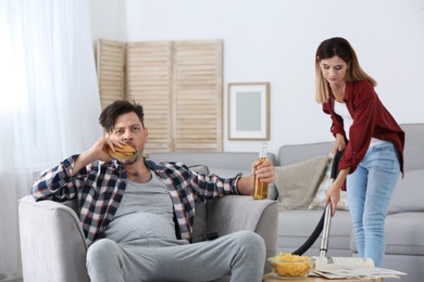 Lazy husband watching TV and his wife cleaning at home
