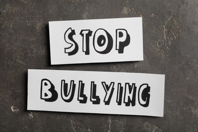Photo of Pieces of paper with text Stop Bullying on grey stone surface, flat lay