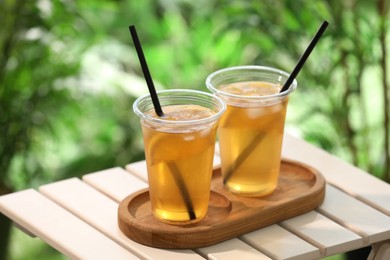 Photo of Plastic cups of tasty iced tea with lemon on white wooden table against blurred background