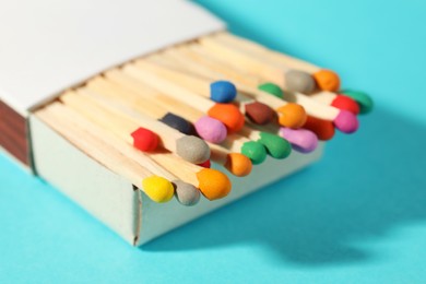Photo of Matches with colorful heads in box on light blue background, closeup