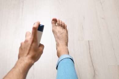 Young man using foot deodorant at home, closeup. Space for text