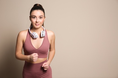 Young woman in sportswear with headphones running on beige background. Space for text