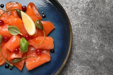 Salmon carpaccio with capers, cranberries, basil and lemon on grey table, top view