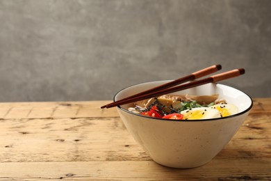 Bowl of delicious ramen and chopsticks on wooden table, space for text. Noodle soup